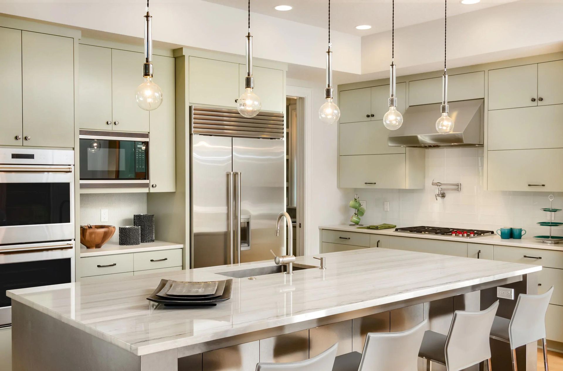 Modern white kitchen with island, pendant lights, stainless appliances, and bar stools