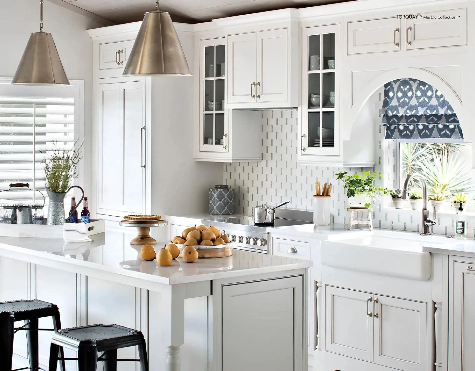 Bright white kitchen with marble island, pendant lights, black stools, and pastries on the counter