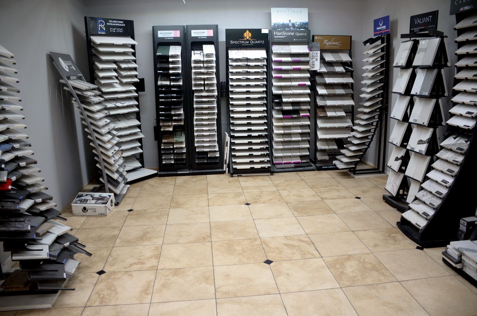 Rows of sample displays and shelving in a carpet store showroom with beige tile flooring