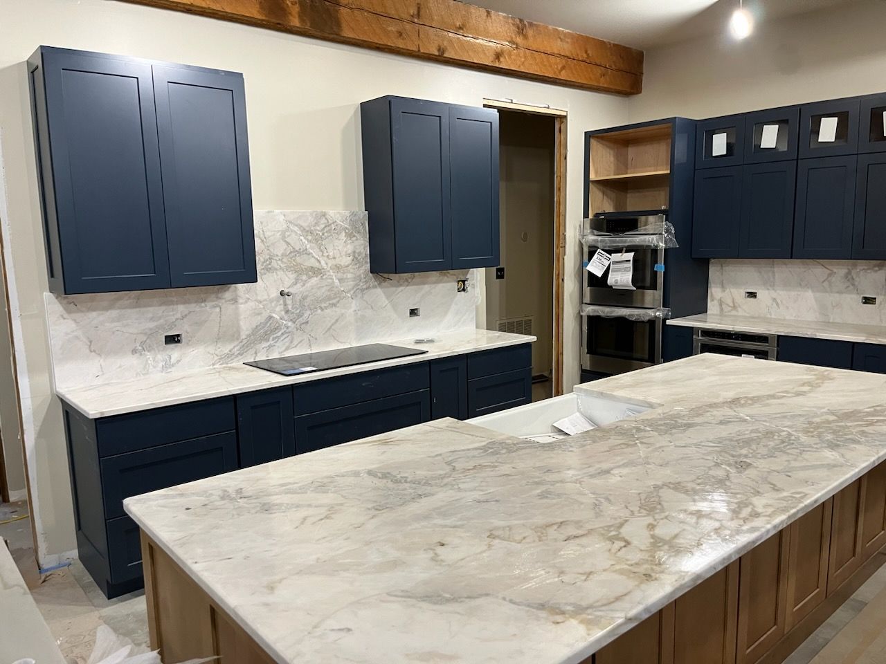 Kitchen with navy cabinets, marble island, white backsplash, and wood beam ceiling