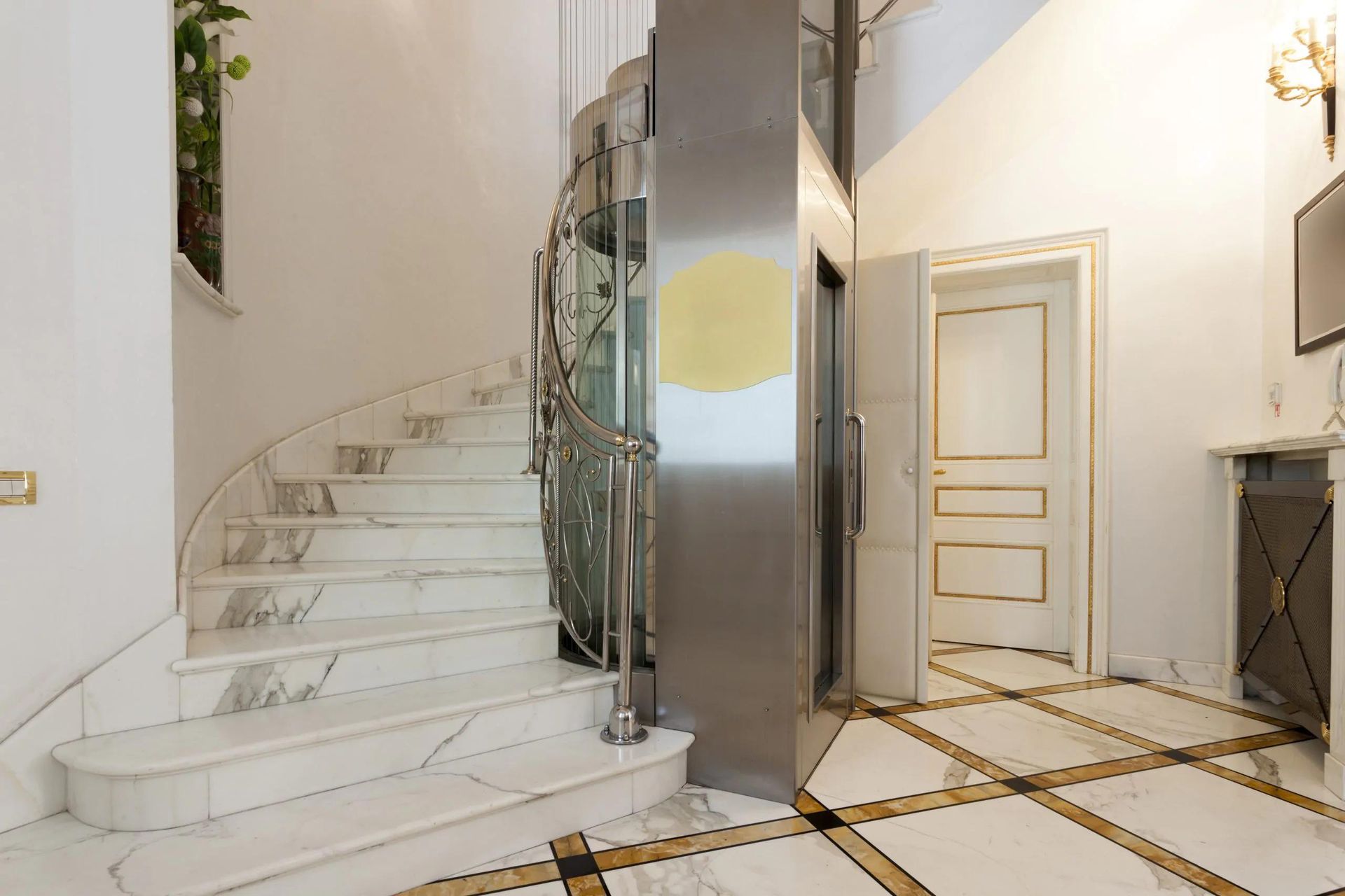 Bright white foyer with curved marble staircase, glass railing, and gold-trimmed tiled floor