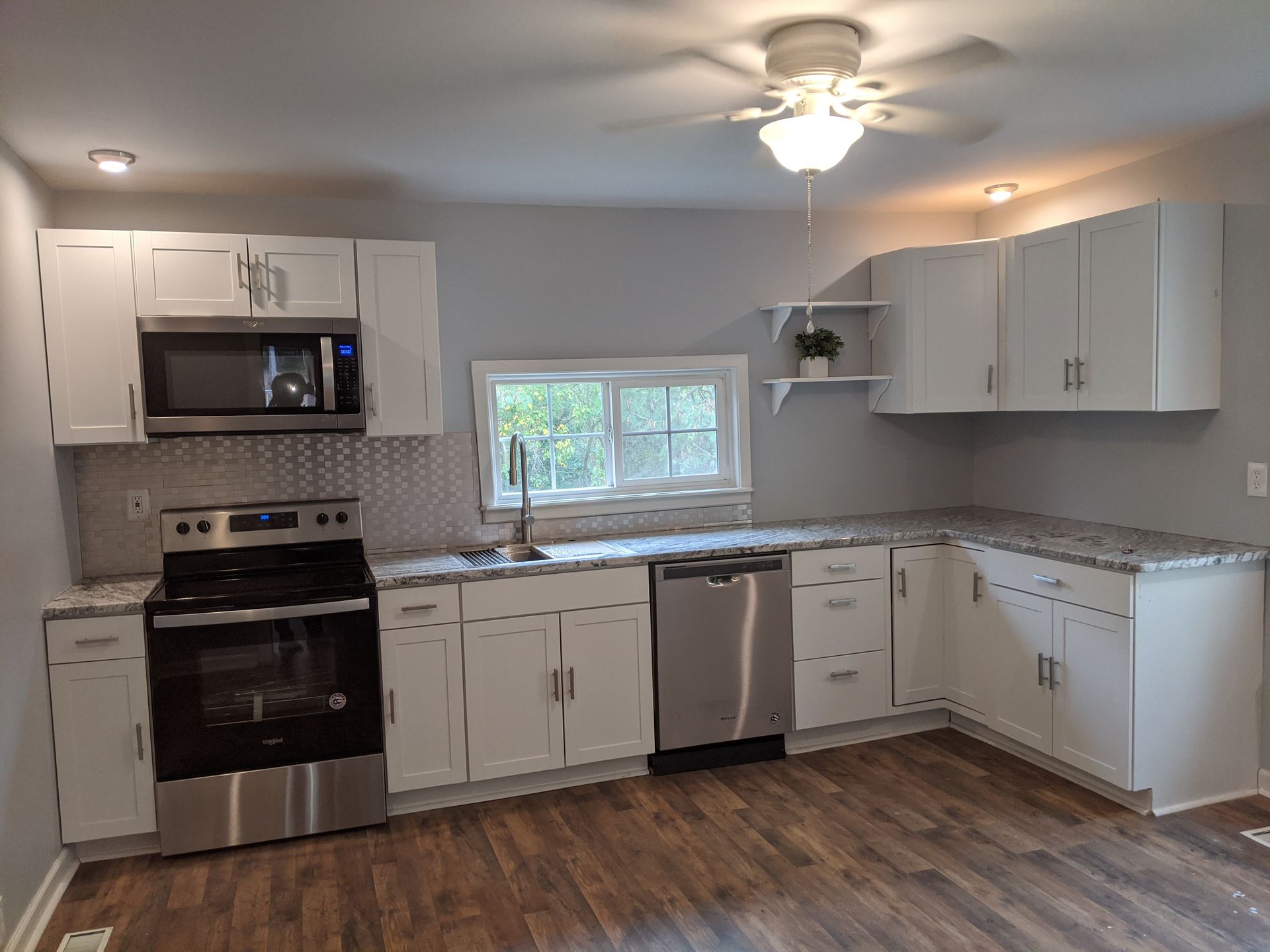 Bright white kitchen with stainless appliances, wood floor, and a window over the sink.