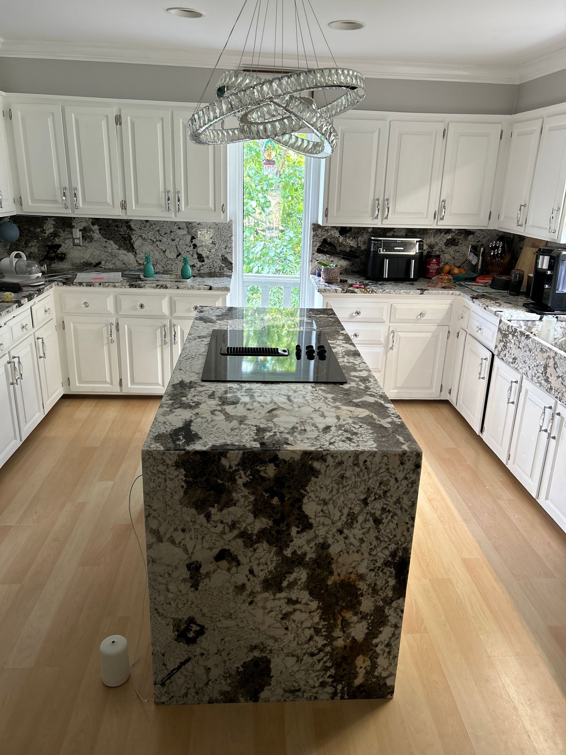 Bright kitchen with white cabinets and a large granite island under a chandelier