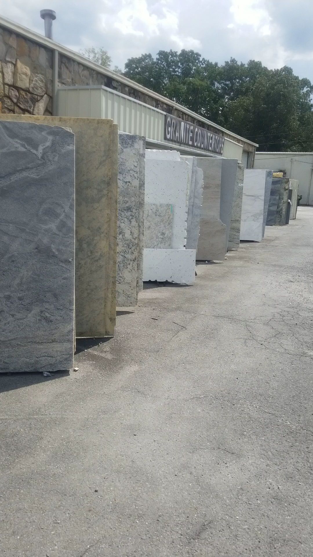 Outdoor stone yard with large granite slabs and tiles lined up along a gravel path