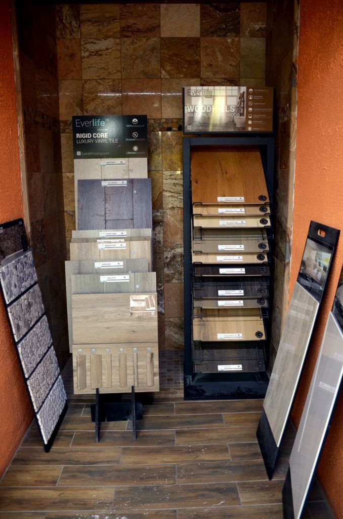 Display racks of flooring samples in a showroom with wood-look tiles and planks.