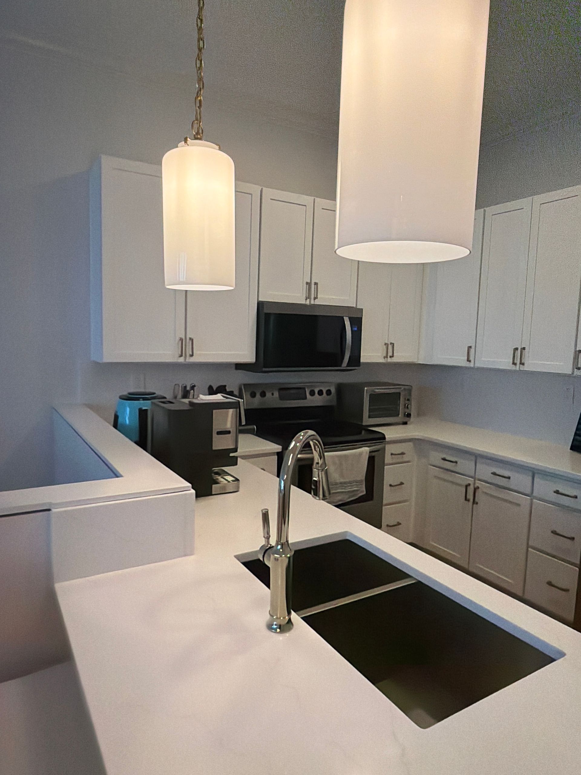 Modern white kitchen with island sink, pendant lights, and stainless steel appliances