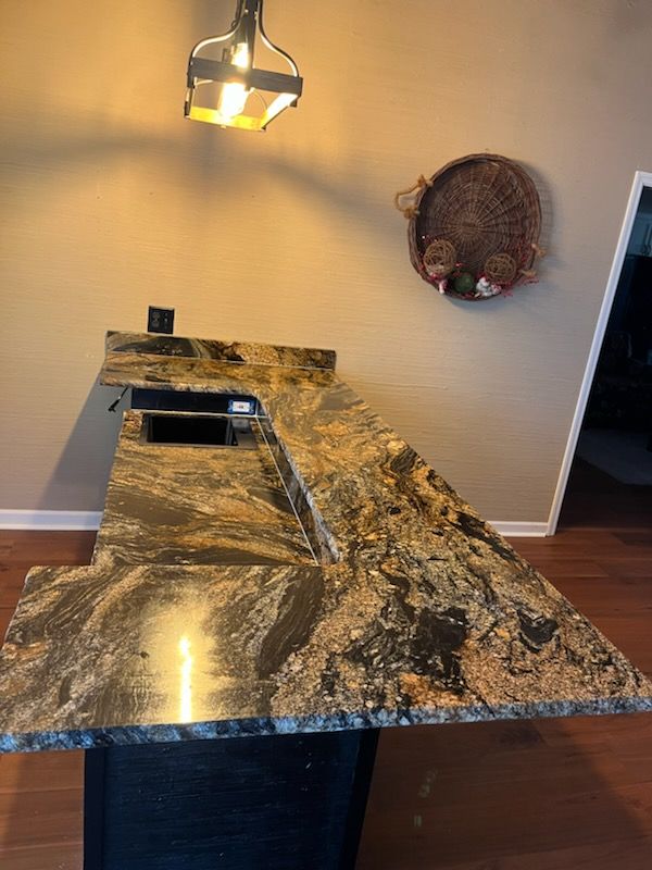 Modern kitchen island with black-and-gold marble countertop, pendant light, sink, and round wall decor