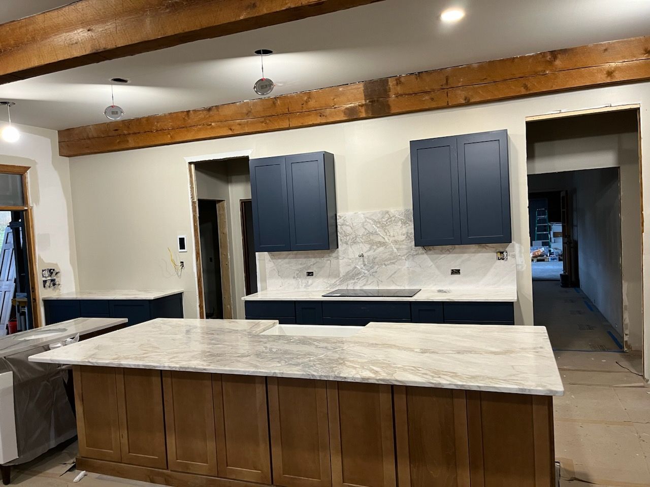 Modern kitchen with navy cabinets, white marble countertops, and a large wooden island under exposed beams