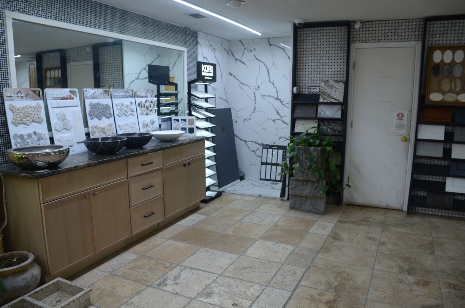 Indoor lobby with beige tile floor, counter displays on the left, white door, and potted plant by the wall