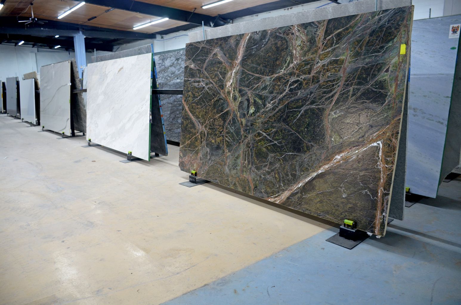 Large stone slabs stored upright in an industrial warehouse, one dark slab in the foreground