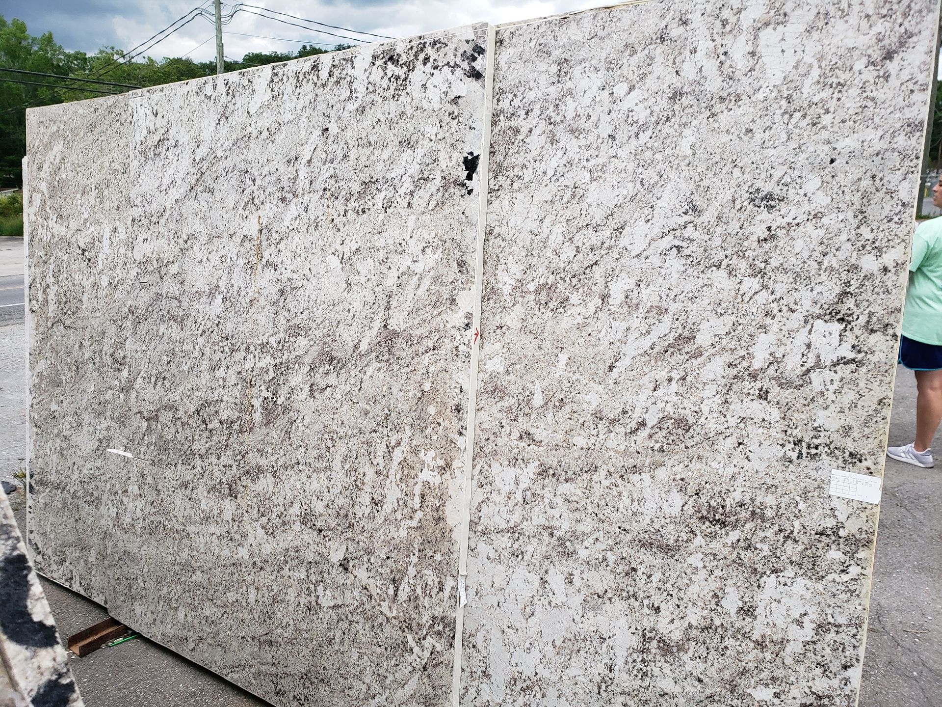Large speckled granite slabs standing outdoors beside a paved path and greenery