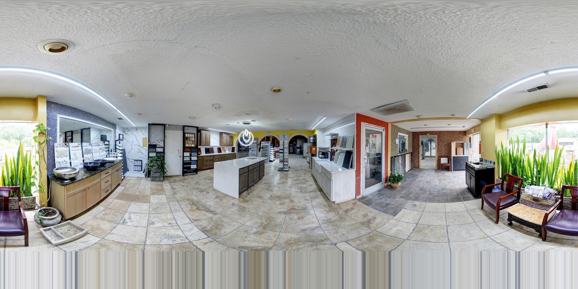 Panoramic view of a bright, modern indoor lobby with tile floors, seating, plants, and reception areas