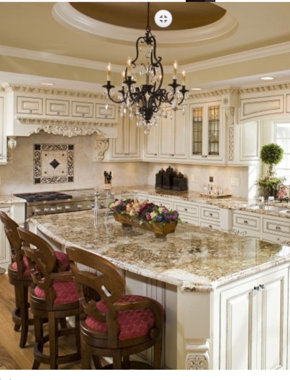 Elegant cream kitchen with marble island, ornate chandelier, and barstools