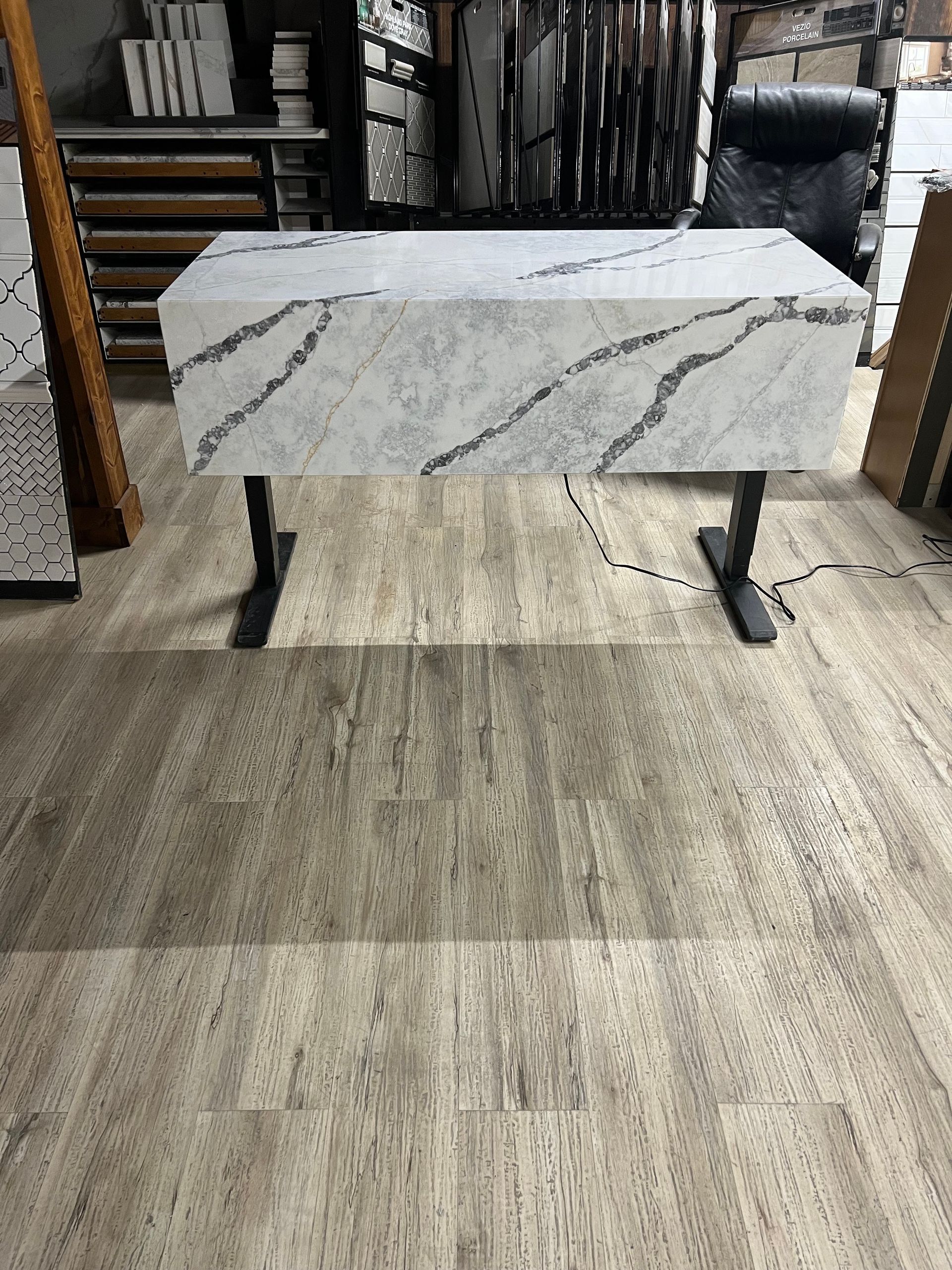 White marble slab on black metal stands in a showroom, with flooring samples around it.
