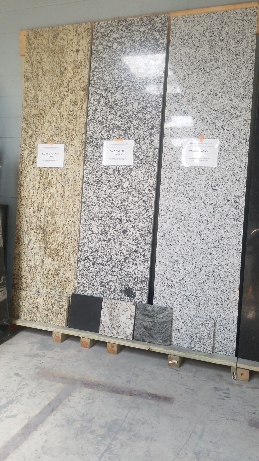 Three upright stone slabs on pallets in a warehouse, with beige and speckled gray surfaces.