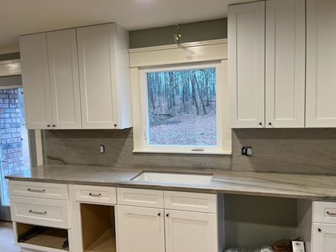 White kitchen cabinets, long countertop, and a window looking out to trees