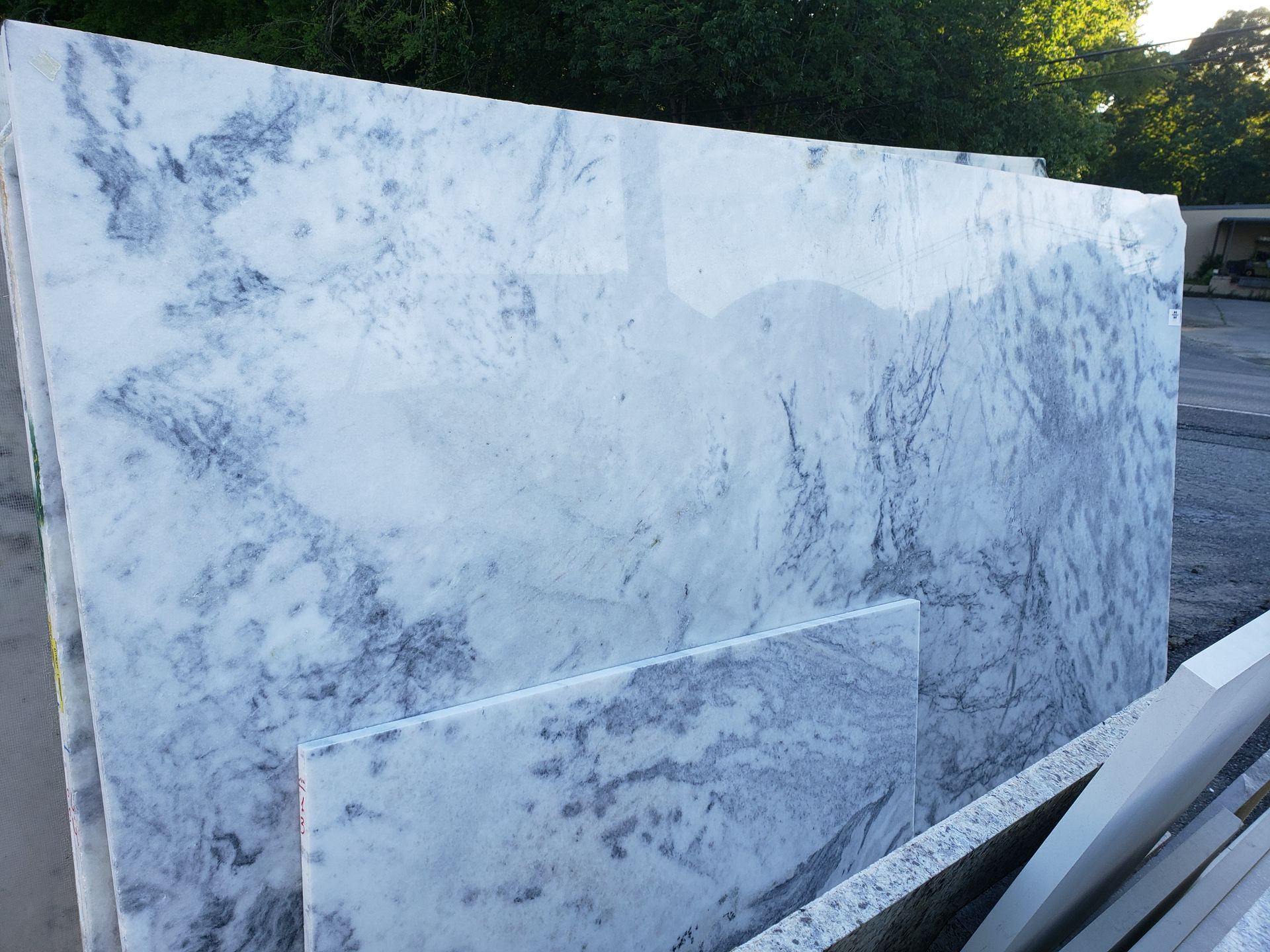 Stacked large marble slabs outdoors, with a white and gray polished slab in front.