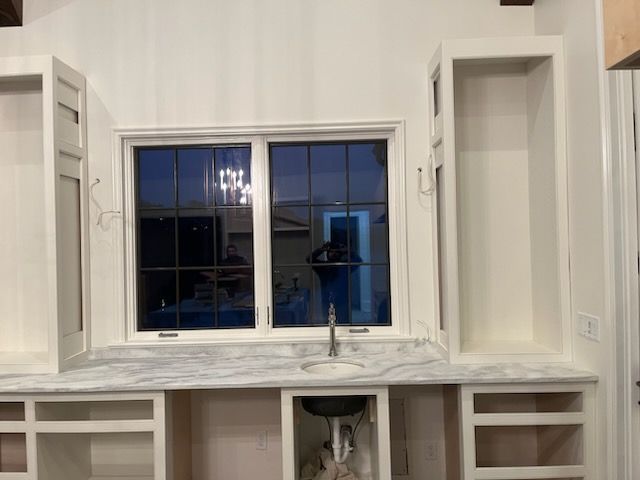 White kitchen with marble countertop, centered window, and built-in shelving on both sides.