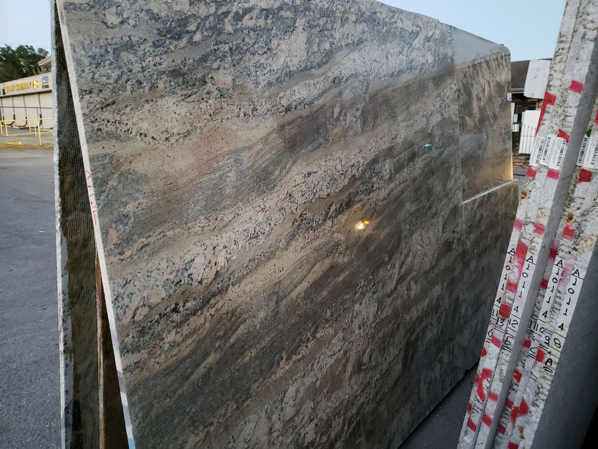 Large polished granite slab with gray, brown, and black veining outdoors on a rack