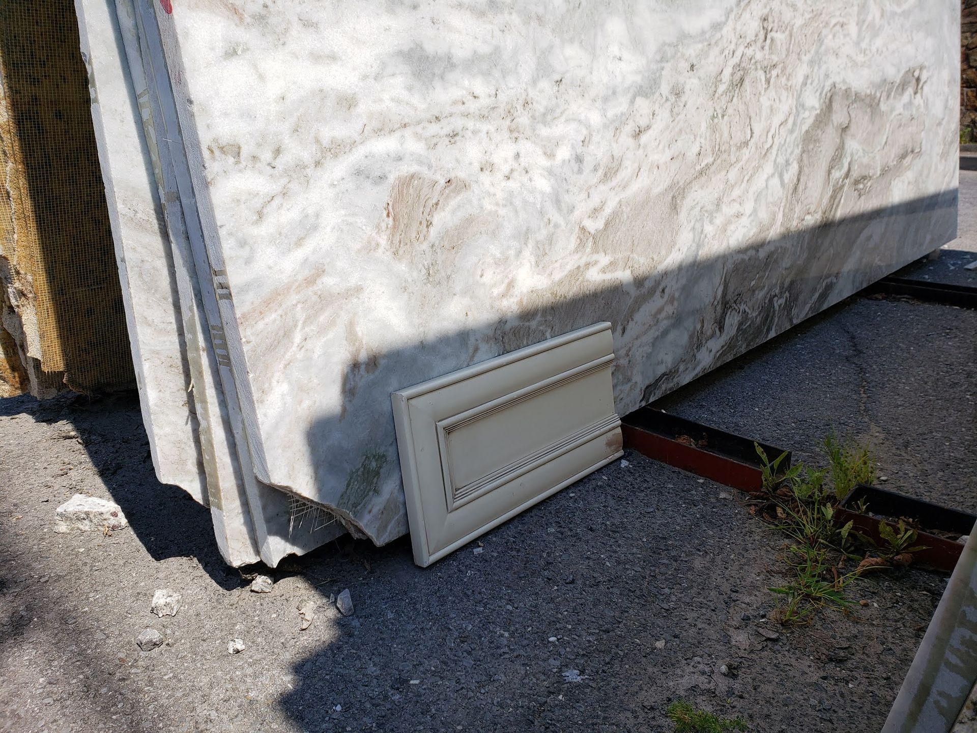 White vent cover leaning against a stone wall beside a paved outdoor area.