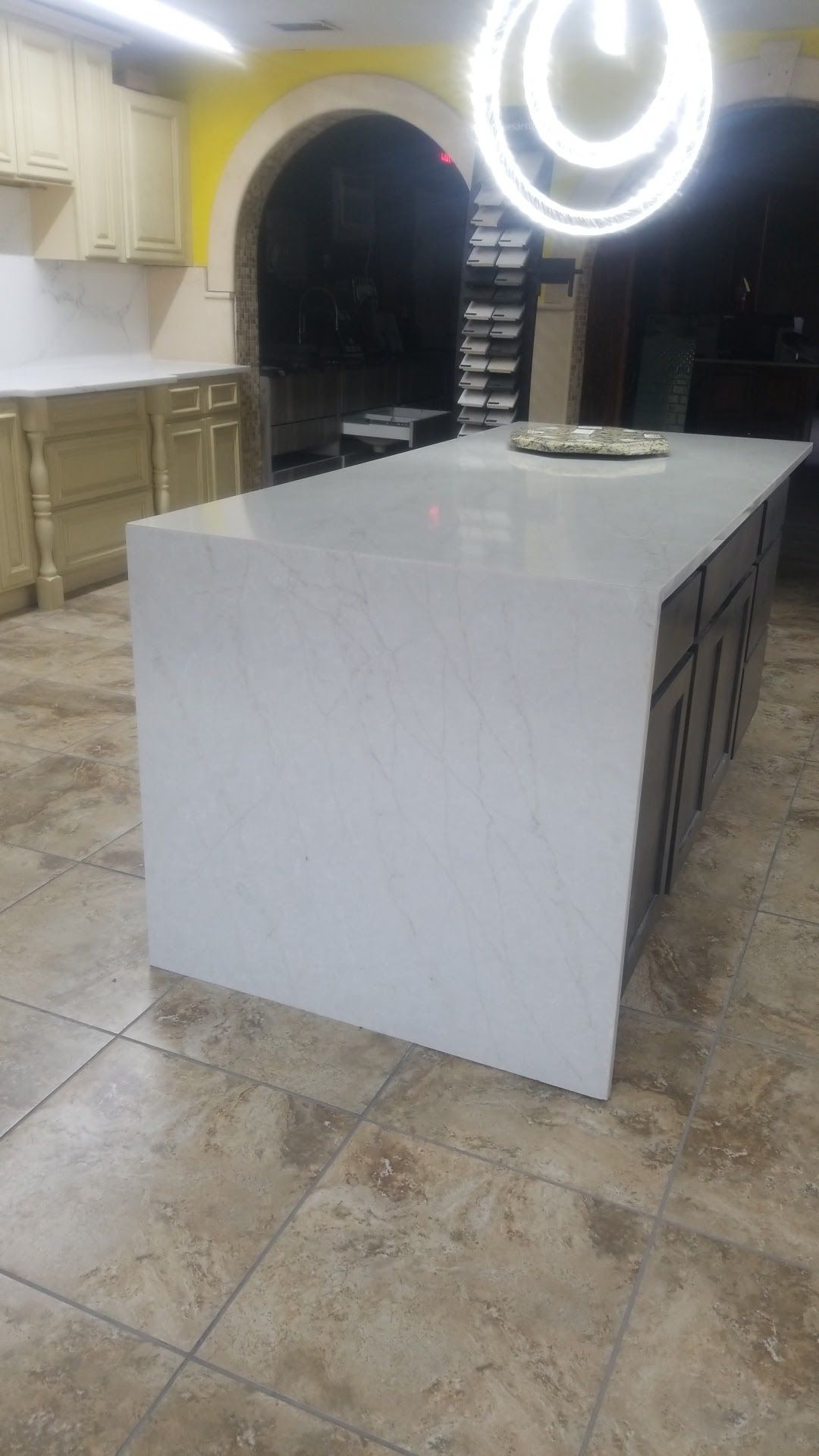 Modern kitchen with a large white island under a circular pendant light and stone tile floor