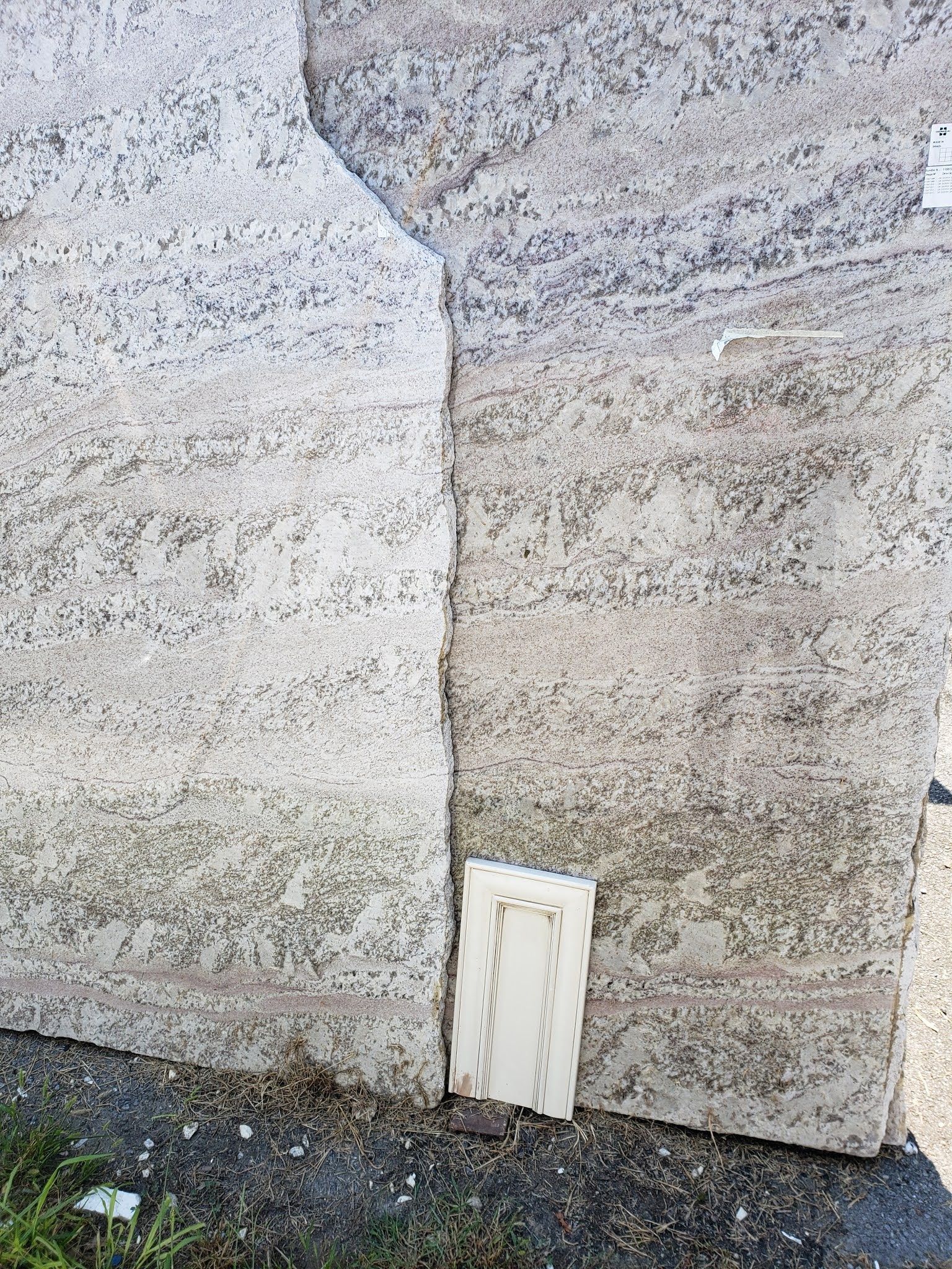 Two stone walls meeting at a corner with a small white utility hatch near the ground.