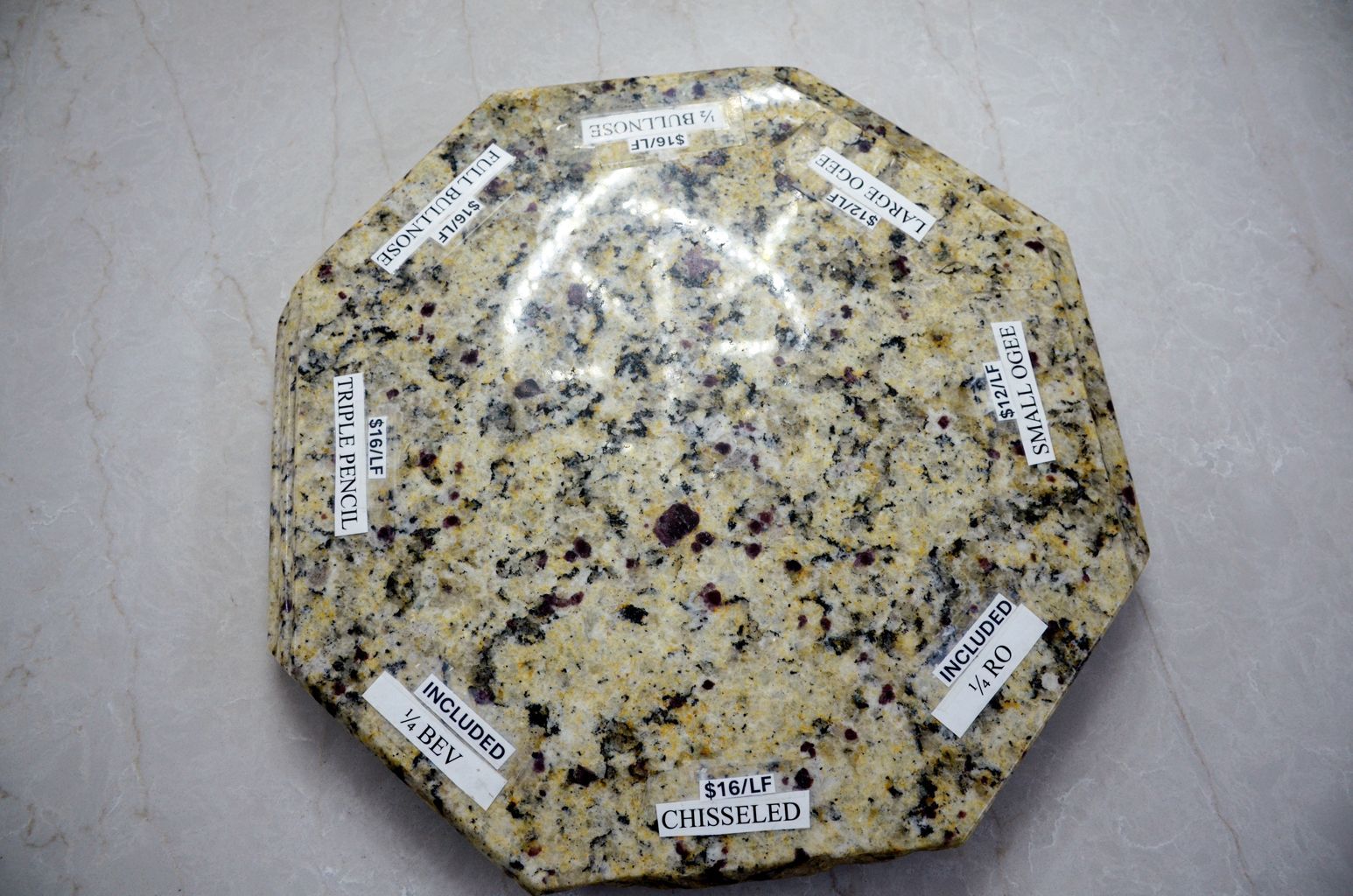 Octagonal speckled granite sample with white labels on a gray floor
