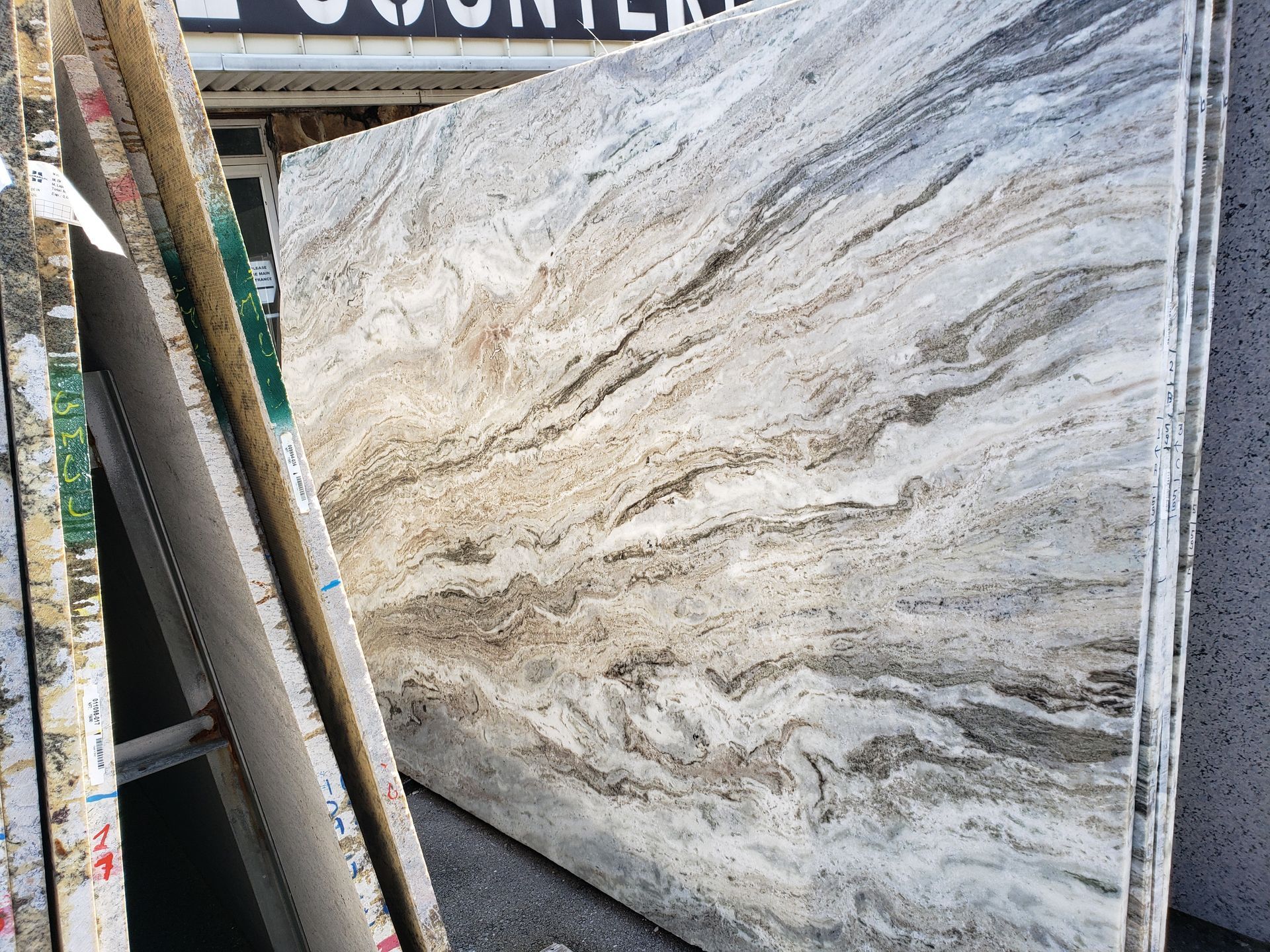 Stacked patterned stone slabs in a warehouse, with a large white and gray veined slab in front.