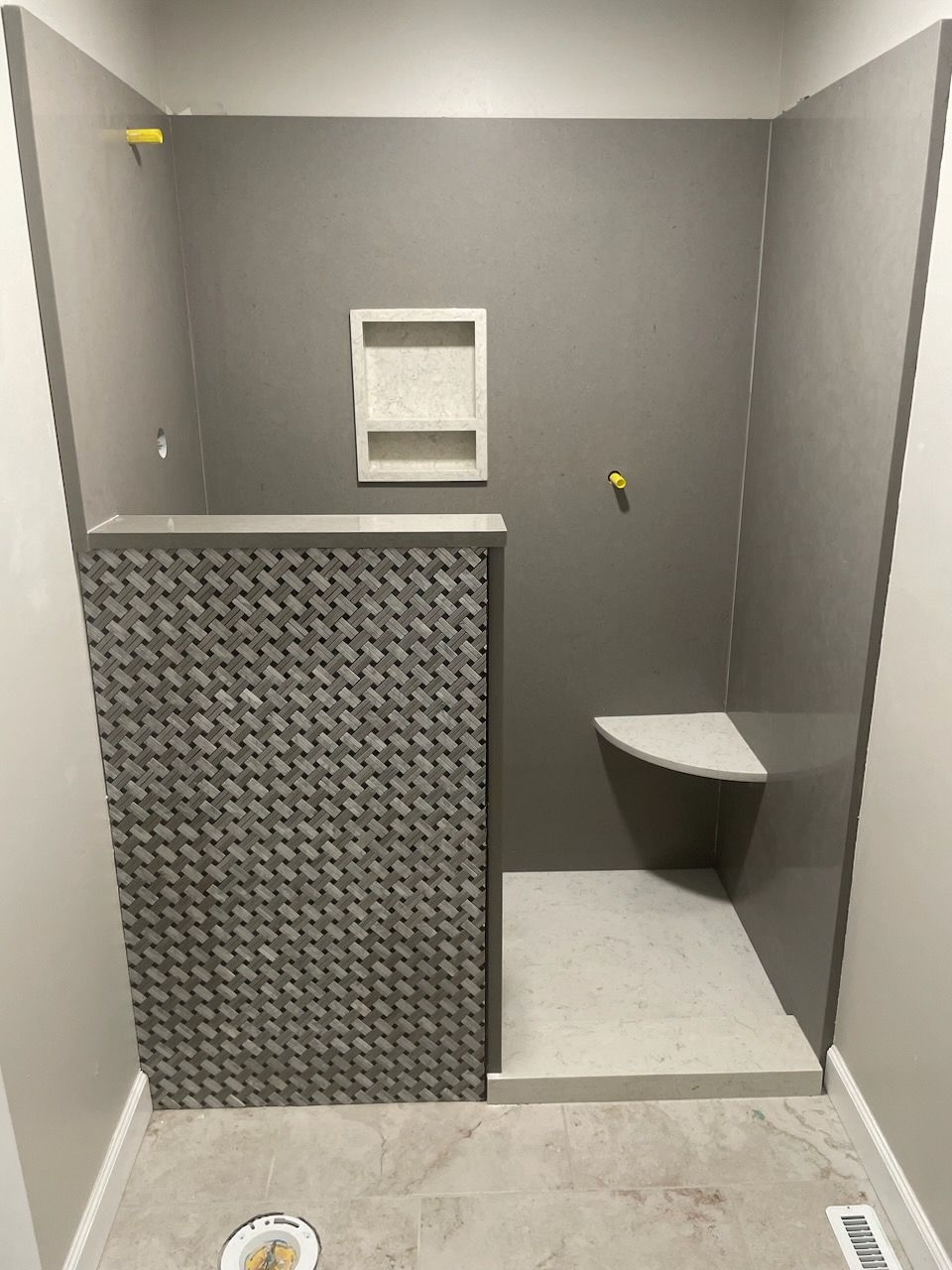 Small gray tiled bathroom with a partition, wall niche, and corner toilet.
