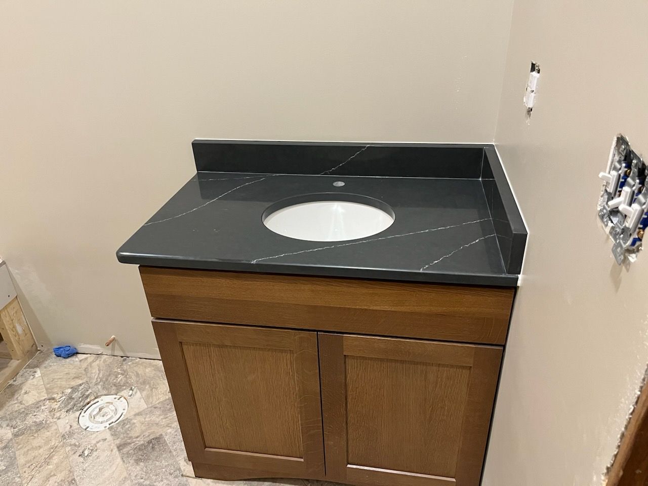 Bathroom vanity with black countertop, oval sink, and unfinished wood cabinet in a partially renovated room