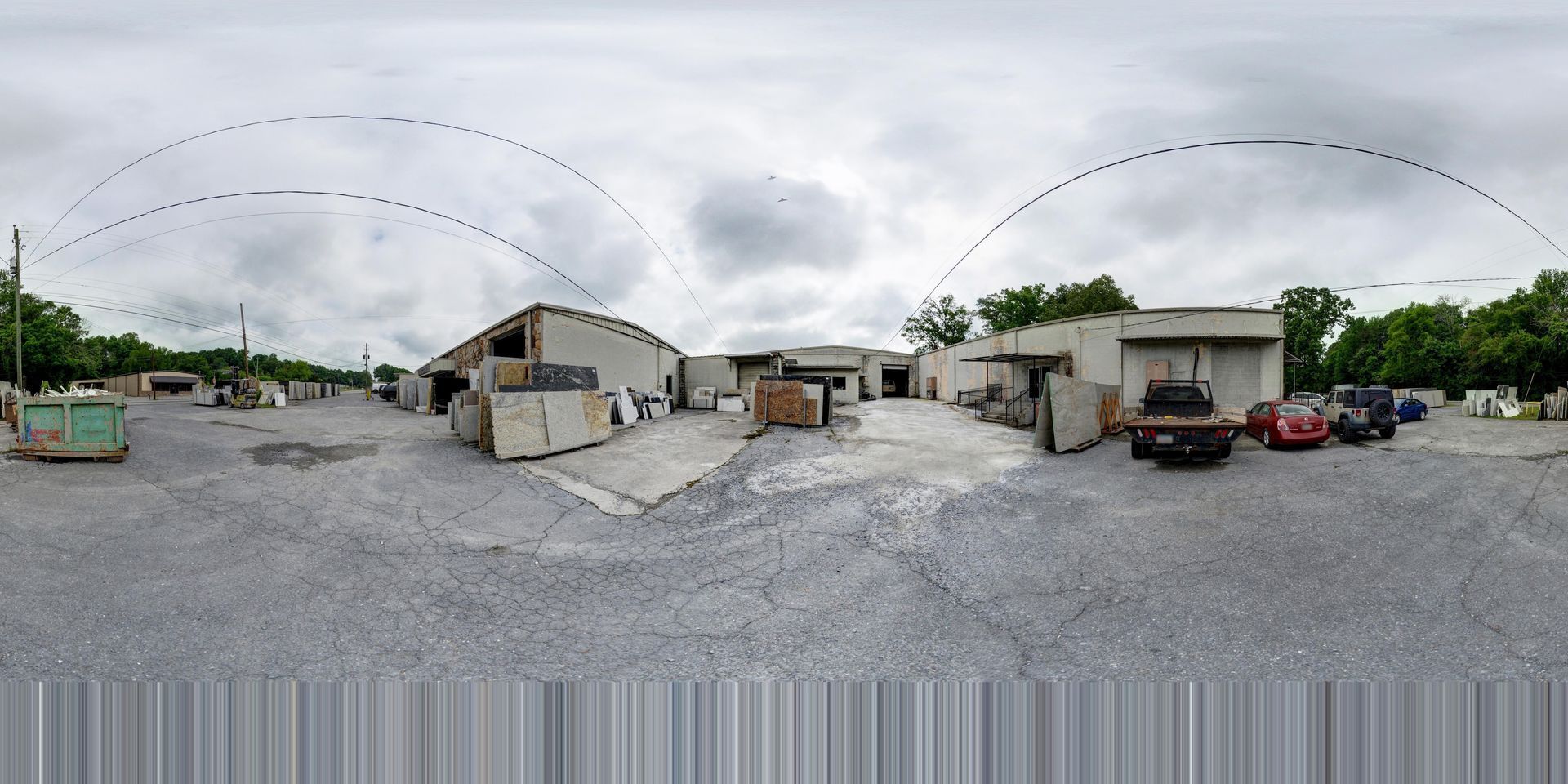 Wide gravel lot with small buildings, parked cars, and an overcast sky