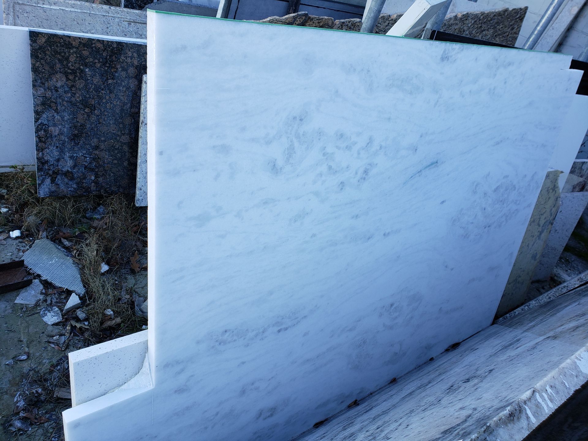 Stacked white marble slabs leaning outdoors beside a dark granite slab and rubble
