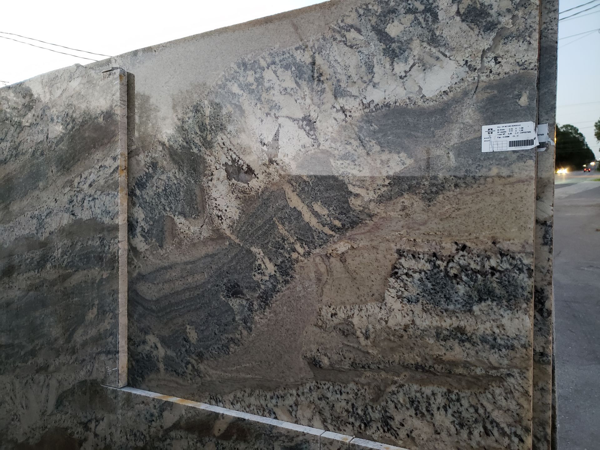 Large stone slab with a mottled gray-brown surface standing outdoors near a roadway.
