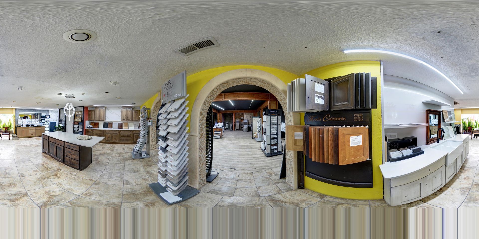 Wide-angle interior of a showroom with wood cabinets, stone archways, and bright overhead lighting