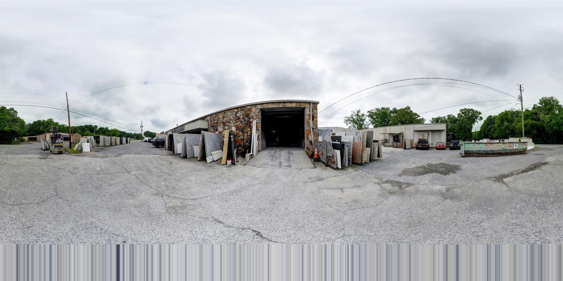 Wide gravel yard with a large open storage shed, scattered industrial equipment, and cloudy sky