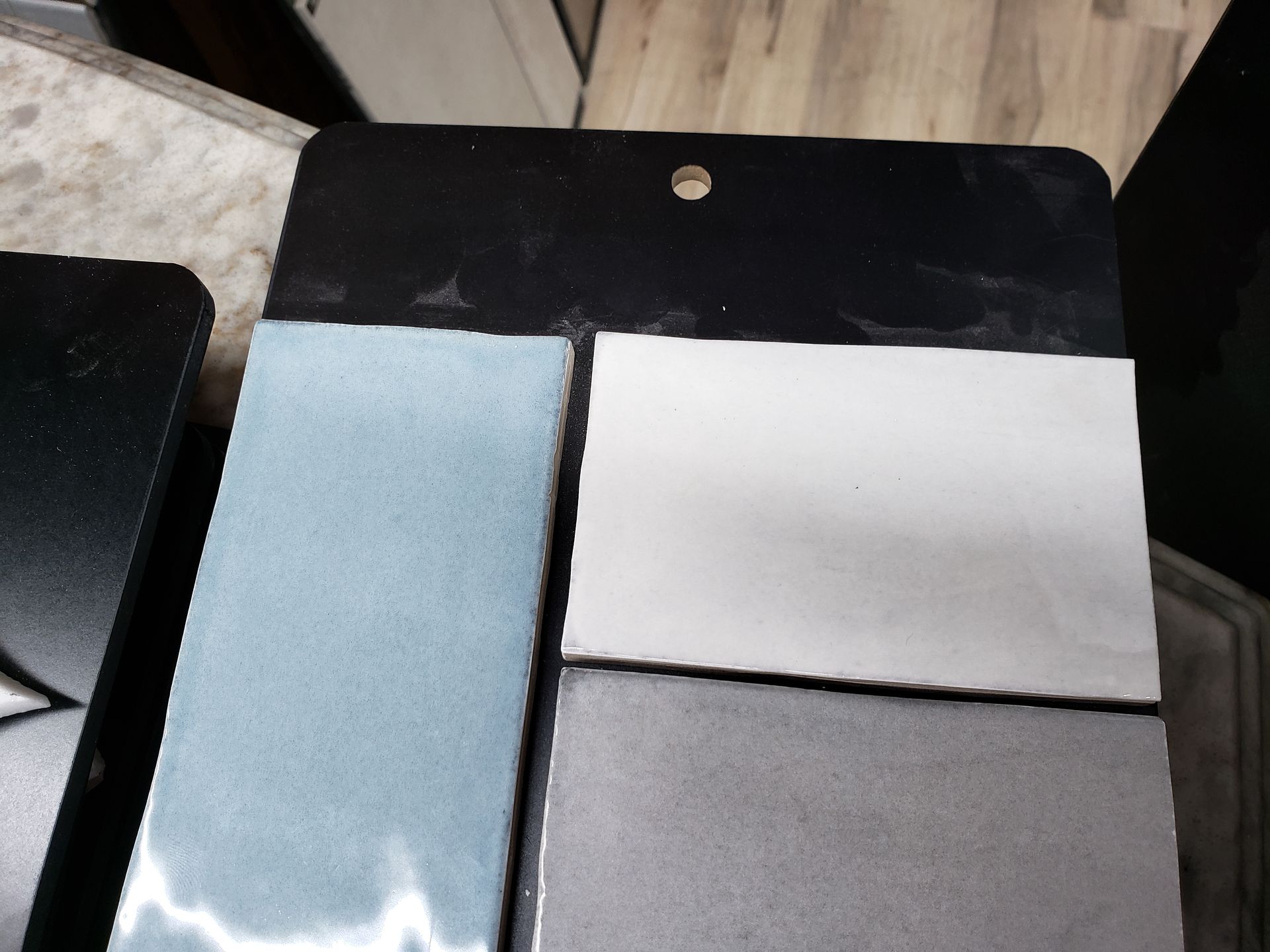 Three rectangular fabric swatches: light blue, white, and gray on a black board