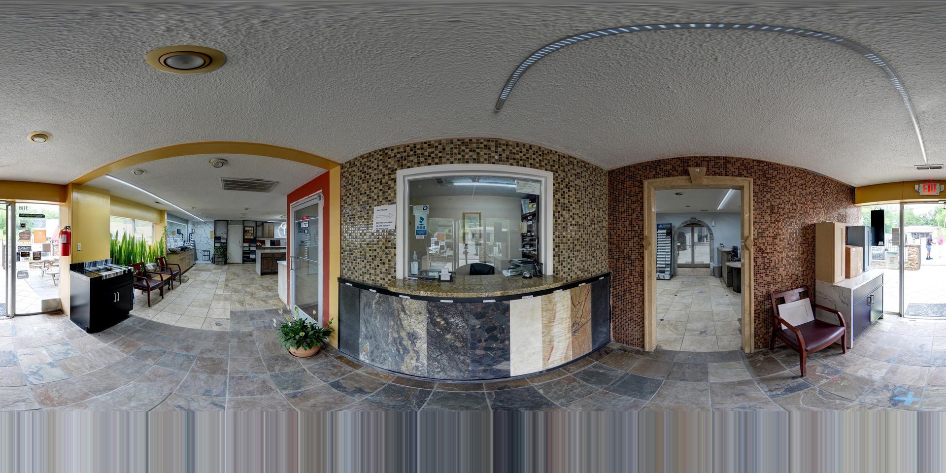 Wide lobby with stone counters, glass windows, tiled floor, and potted plants under an arched ceiling.