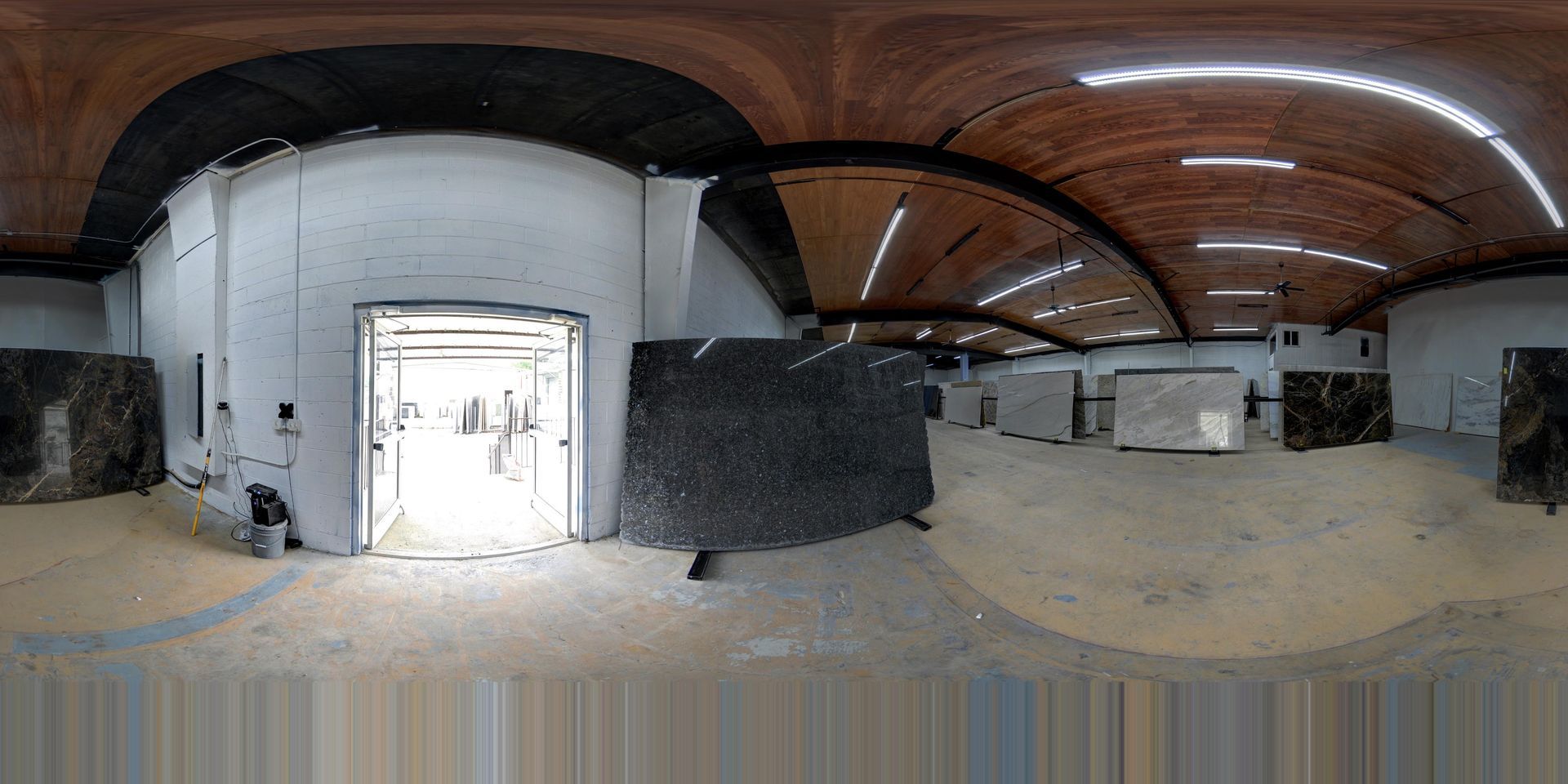 Wide-angle view of an unfinished industrial interior with a white doorway, sand-covered floor, and arched wooden ceiling