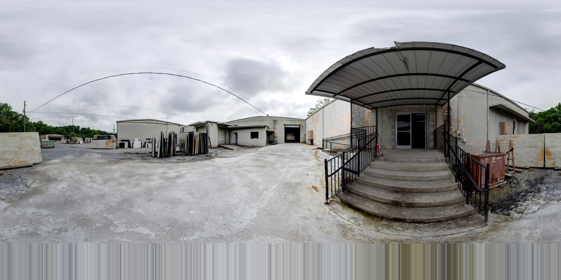 Wide gravel courtyard with white buildings under a cloudy sky, seen from a front porch with steps and railing
