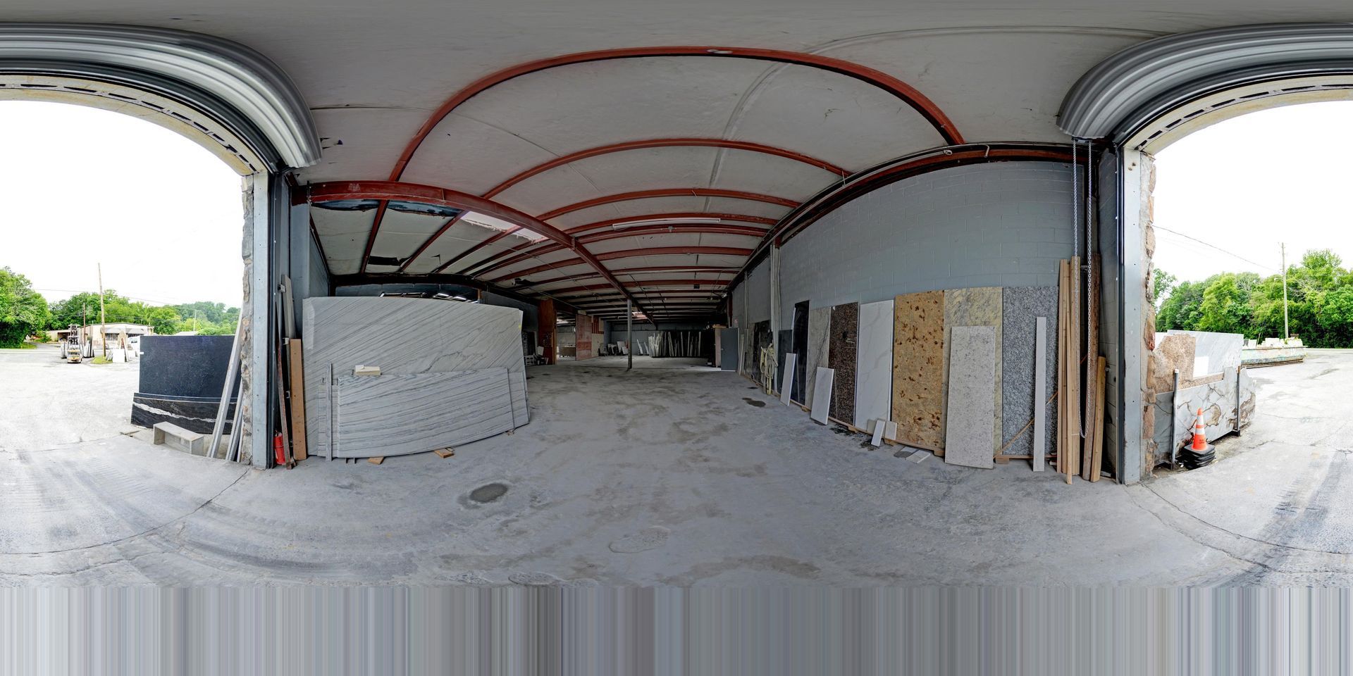 Empty unfinished indoor space with curved ceiling beams and construction materials, open to greenery outside