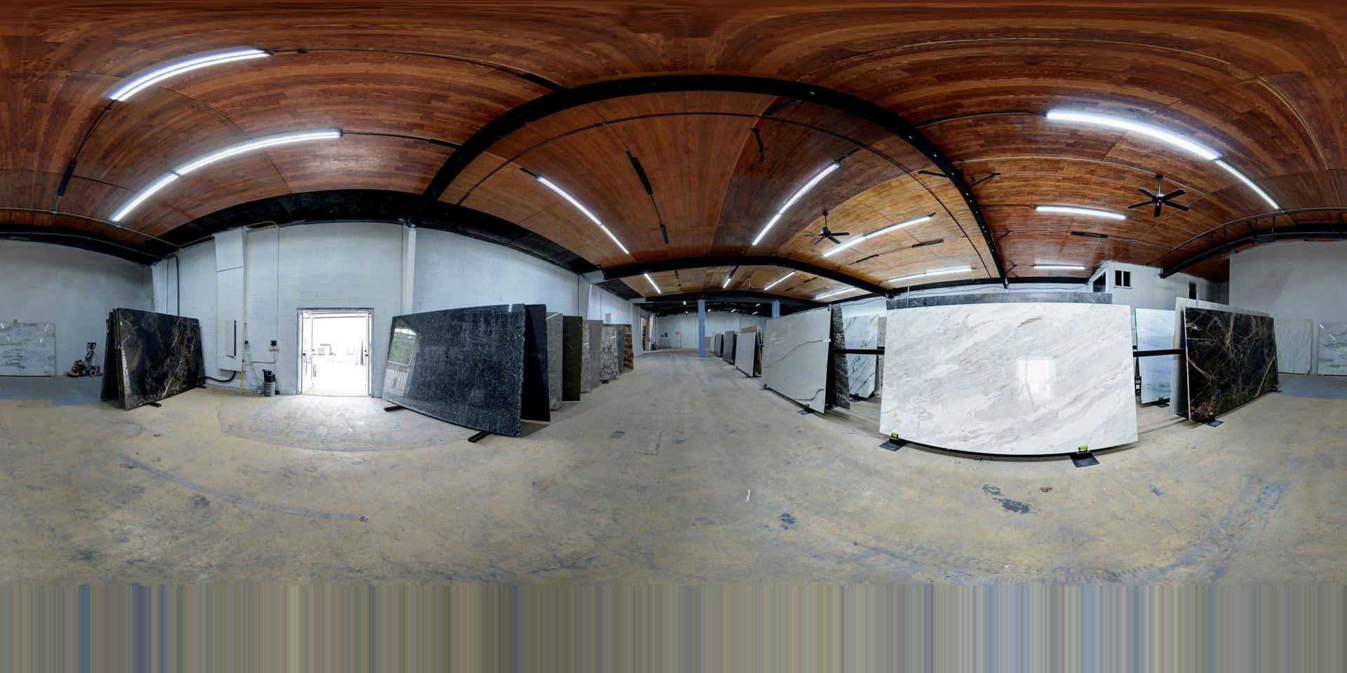 Wide warehouse interior with curved wooden ceiling, concrete floor, and several white-covered structures.