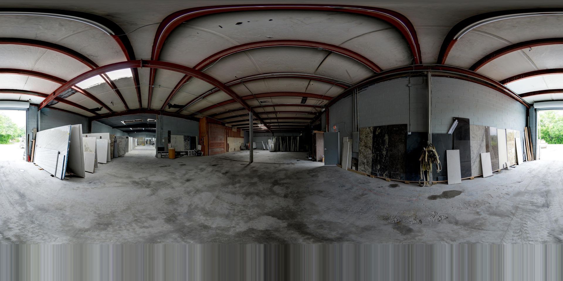 Wide-angle view of an empty industrial warehouse with arched red ceiling beams and concrete floor
