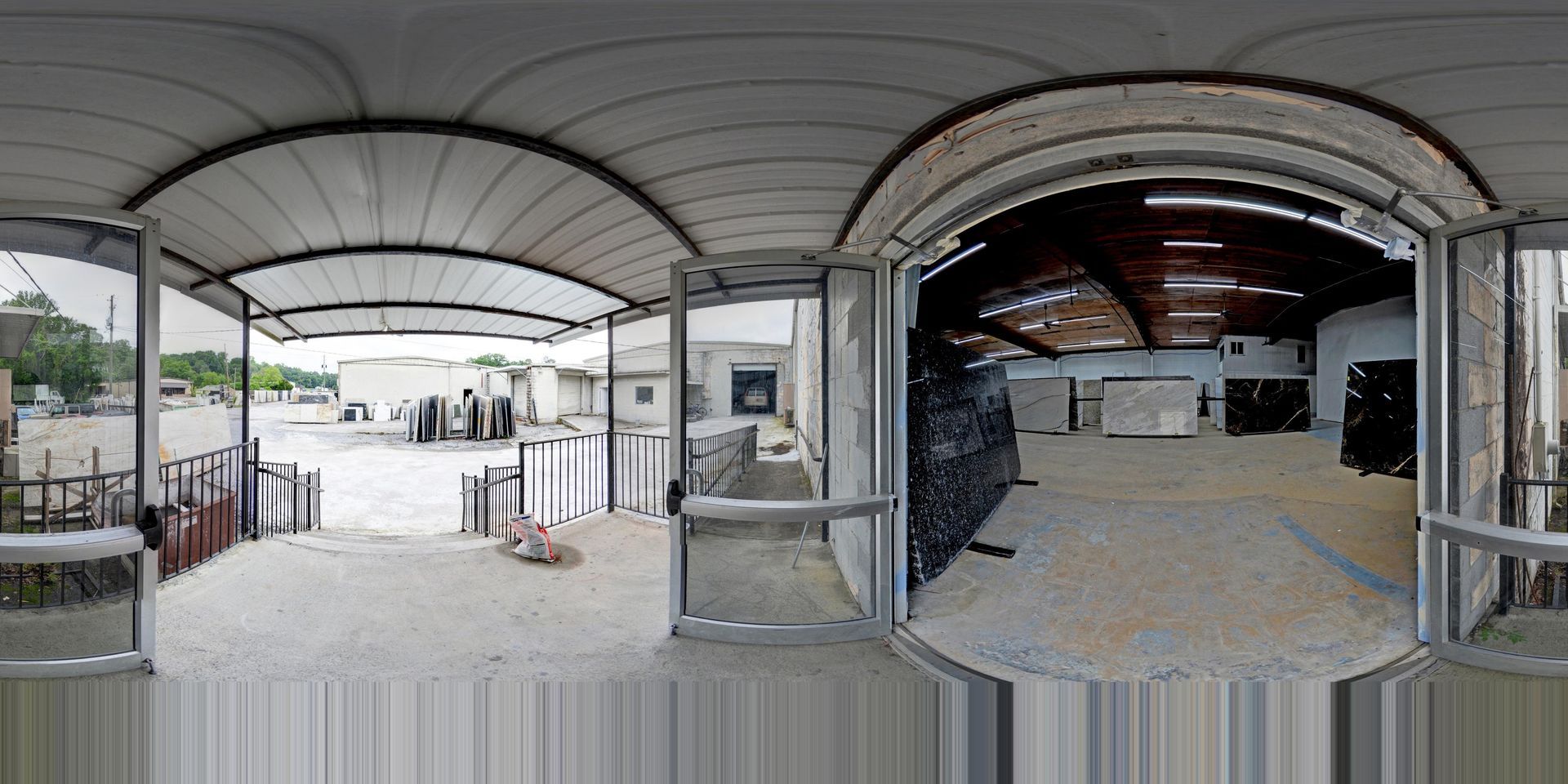 Industrial warehouse entrance with curved roof, open doors, and stacked materials inside and outside
