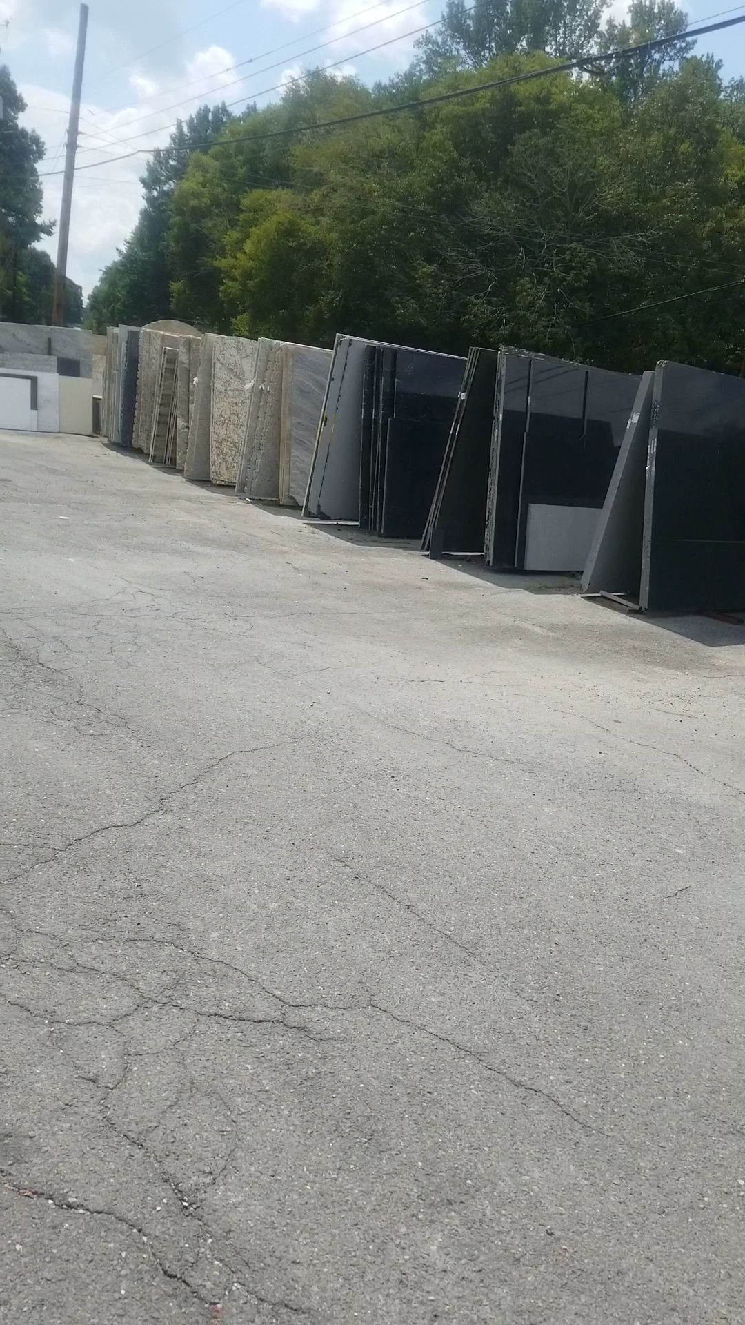 Row of large dark dumpsters and containers along a gravel lot with trees and utility poles in the background