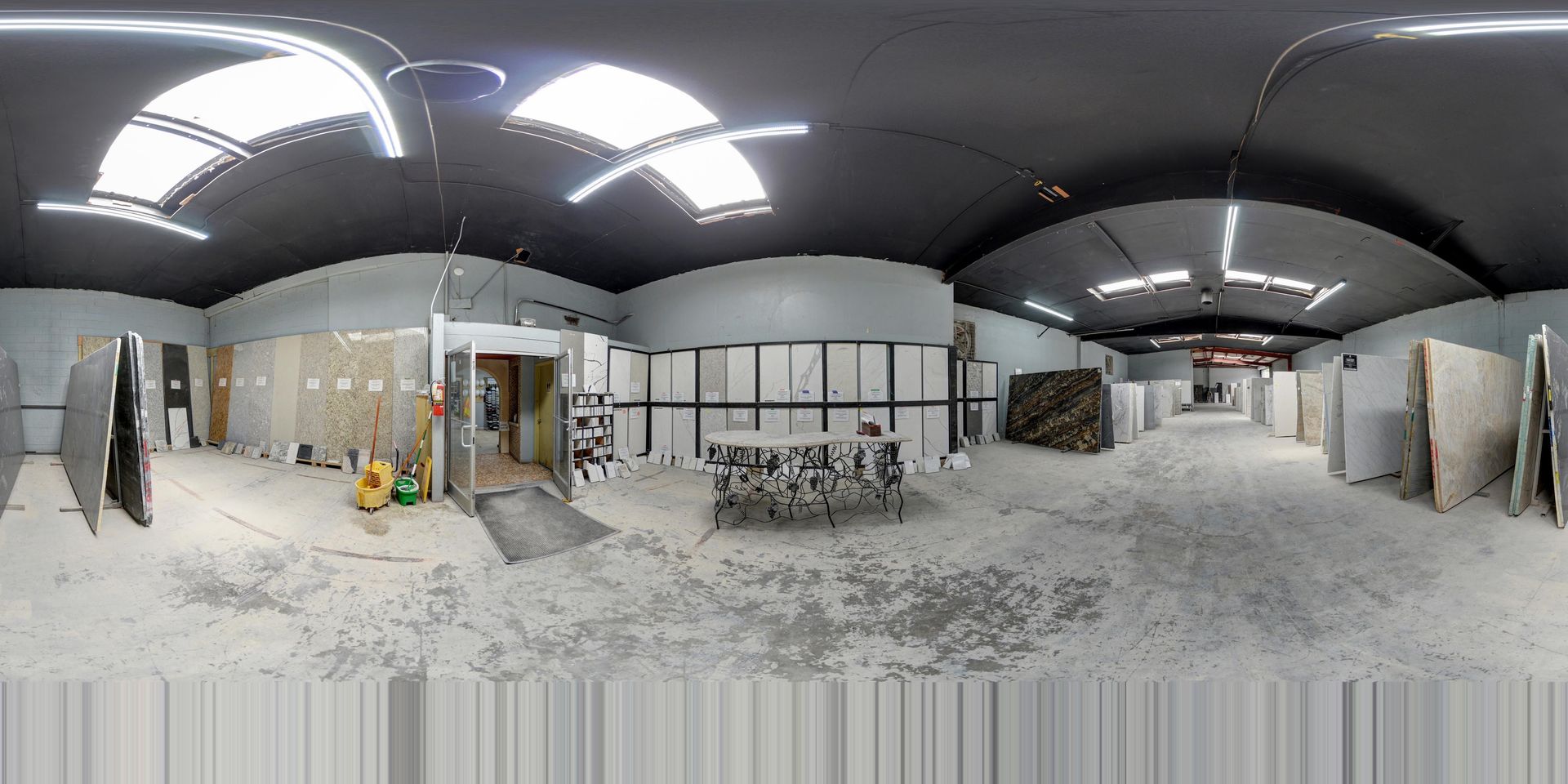 Panoramic view of a dusty construction site with exposed walls, lights, and scattered materials inside a large room