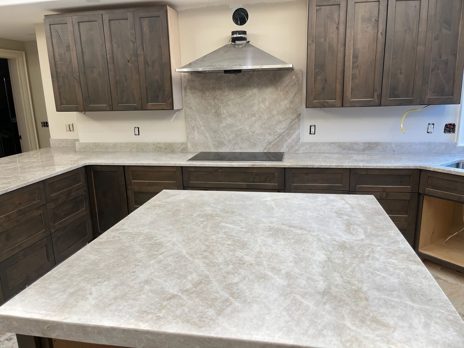 Modern kitchen with dark cabinets, light stone countertops, and a central island under a stainless steel range hood