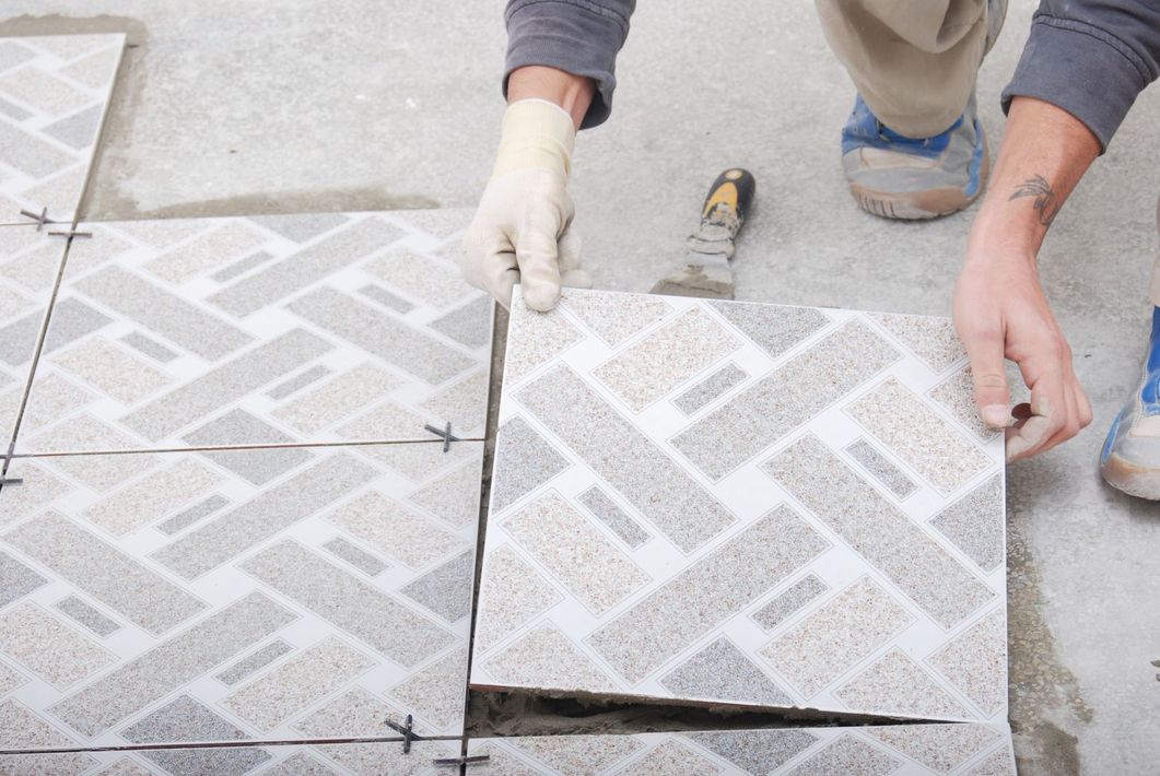 Two people laying white patterned paving tiles on a concrete walkway with tools nearby
