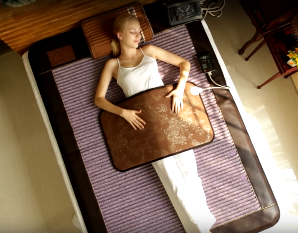 A woman is laying on a bed with a brown blanket on her stomach