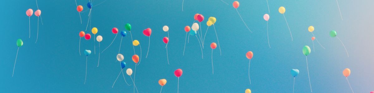 Colorful balloons floating in a blue sky with a few dangling strings