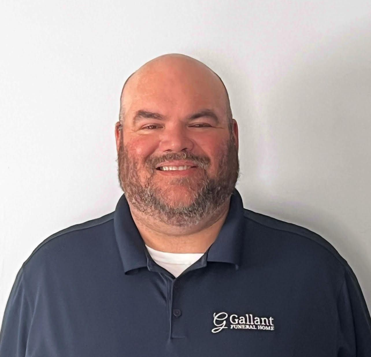Smiling man in navy polo shirt standing against a white background